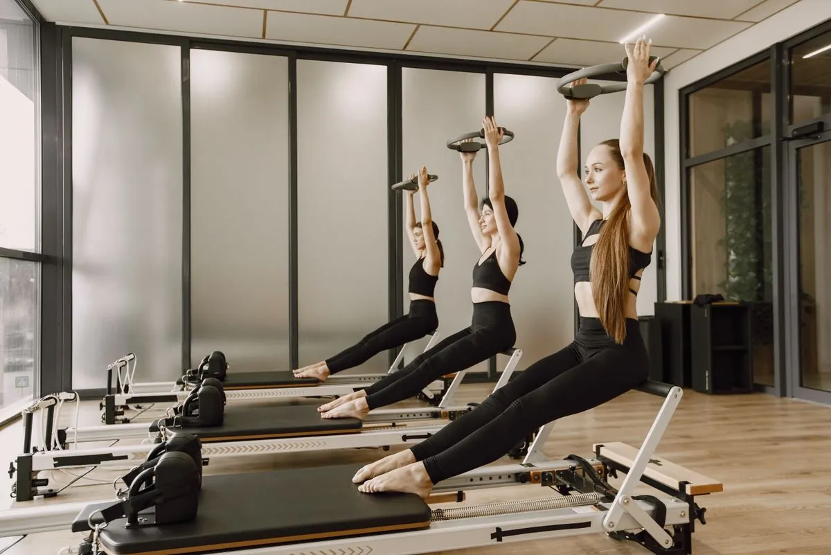 Three people on reformers lifting their arms in unison